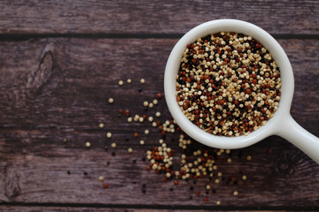 Quinoa seeds in the white cup on wooden background.  Quinoa is a good source of protein for people following a plant-based diet. 