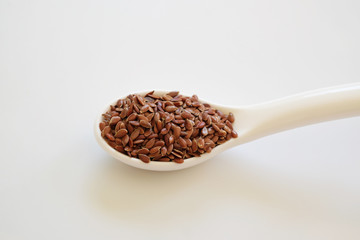 Brown Flax seeds or Linseeds or Common flax in the white spoon isolated on white background. Flax seeds are rich of omega fat.