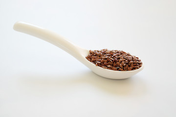 Brown Flax seeds or Linseeds or Common flax in the white spoon isolated on white background. Flax seeds are rich of omega fat.