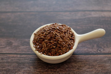 Brown Flax seeds or Linseeds or Common flax in the white bowl isolated on wooden background. Flax seeds are rich of omega fat.