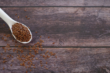 Brown Flax seeds or Linseeds or Common flax in the white spoon isolated on wooden table background. Flax seeds are rich of omega fat.
