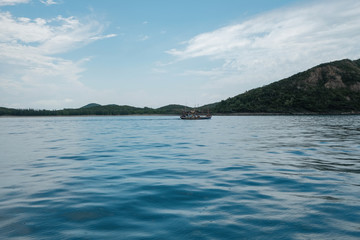 The boat is sailing at sea with mountain and blue sky background.