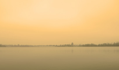 Yellow sunset over the lake in the fog