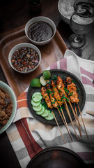 chicken satay view from above on stiped napkin and wooden tray also with two bowl of sauce