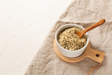 Cannabis kernels in a white bowl with a wooden spoon on a linen napkin on a white table
