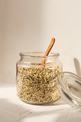 Cannabis kernels in a glass jar on a white table with a wooden spoon