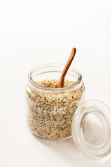 Cannabis kernels in a glass jar on a white table with a wooden spoon