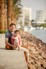 Fototapeta na wymiar Son & father walking on a beach near palm trees weared in casual clothes. Tropic vacation. Sea relax and rest. Spending a time on a beach. Smiling boy with his Dad together. Summer holiday sunny day
