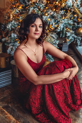 girl in a bright red festive dress in the house on the background of a Christmas tree and a large window