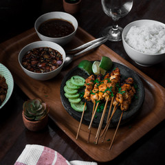 indonesian traditional culinary chicken satay on stone plate and wooden tray with two bowl of sauce and a bowl of rice