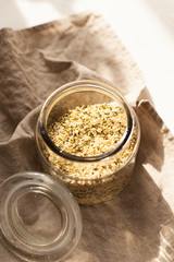 Cannabis kernels in a glass jar on a white table with a wooden spoon