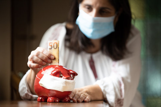 Woman with mask inserting euros into a pig-shaped piggy bank also with mask