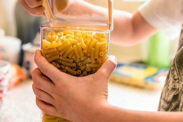 childs hands opening macaroni pasta inside clear storage container on kitchen worktop