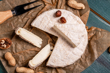 Brie type of cheese. Camembert cheese. Fresh Brie cheese and a slice on a wooden board with nuts. Italian, French cheese. The concept of oriental cuisine. National Italian French product