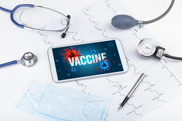 Tablet pc and doctor tools on white surface with VACCINE inscription, pandemic concept