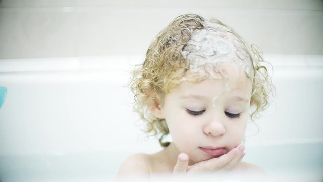 Adorable blonde baby girl washes her face and hair in the bath