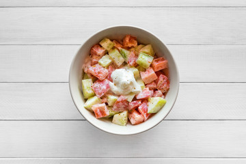 Fresh salad with tomato and cucumber, seasoned with sour cream. Placed on white wooden table. Top view