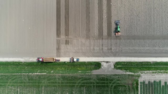 Aerial top down view of farmers working together showing several agricultural machines tractors with implements and one farmer adding materials to the load in a tractor 4k high resolution quality