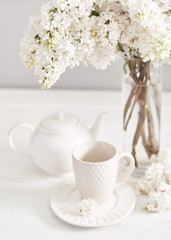 Obraz na płótnie Canvas Bouquet of white lilac in vase and tea set on table in kitchen. Happy birthday greeting card. Hello spring and summer. Greeting card for Women's Day and Mother's Day. Spring season, copy space