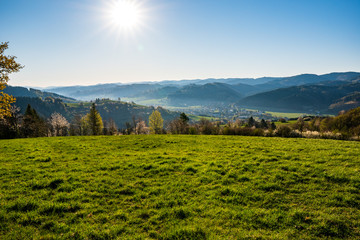 green field in the mountains with a valley below and the sun on the horizon, czech