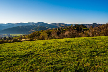 Fototapeta na wymiar green field in the mountains with a valley below and the sun on the horizon, czech