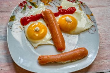 Plate with eggs and sausage in shape of face on wooden background