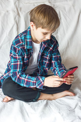A schoolboy boy communicates with his friends via smartphone and social networks during coronovirus quarantine. Home isolation and social distance. Gadget addiction learning online	