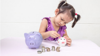 Three years old child is saving money into piggy bank. in white background. saving money for future, dream, education. happy child. stay at home. family activities.