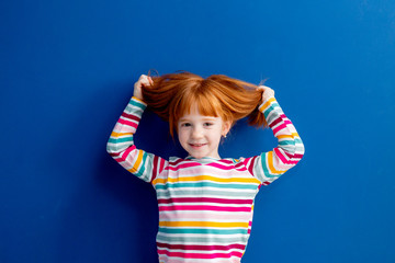 little girl with red hair in a multicolored smile stands on a blue background