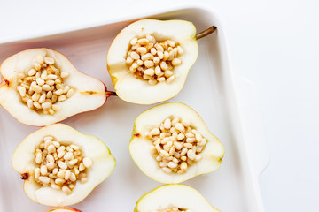 Halved ripe pears stuffed with nuts and honey in a white baking dish.