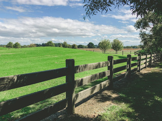 Fototapeta na wymiar Scenic Australian farmland landscape - wooden fence near green hill under blue sky with fluffy clouds