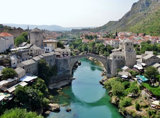 Fototapeta na wymiar Imagen panorámica del icónico Puente Viejo de Mostar con sus torres a los lados sobre las aguas color turquesa del río Neretva