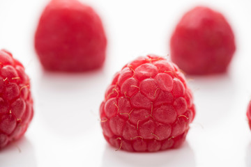 Several fresh raspberries on a white surface with reflection.