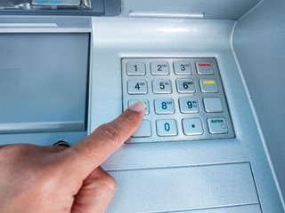 The man is pressing the secret code on the ATM's numeric keypad with the index finger of the left hand.