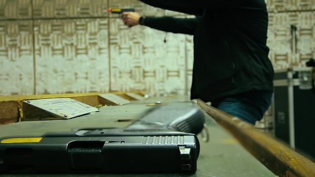 Cinemagraph of two unrecognizable men reload and shoot with a 9mm pistol in shooting range. Close up on a gun in the foreground. Loop, selective focus and copy space.
