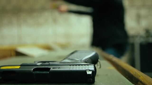 Cinemagraph of two unrecognizable men shoot with 9mm pistol in shooting range. Close up on a gun in the foreground. Loop, selective focus and copy space.