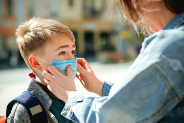 Mother puts a safety mask on her son's face. Schoolboy is ready go to school. Back to school concept.