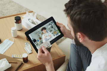 Sick man with tablets and mobile gadget consulting doctor in the net