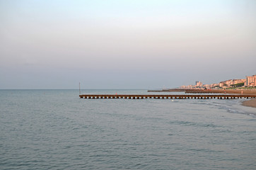 Fototapeta premium Beautiful coastline of the Adriatic Sea. Sunrise on the beach of Lido di Jesolo. Piers in the sea