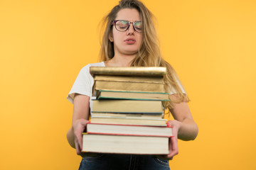 A young girl with glasses holds a pile of books, looks at them skeptically, does not want to study, a boring face