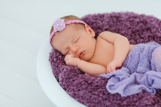 Newborn baby in violet knitted suit sleep in wooden basket. Child resting in cute pose. Tiny girl with tender headband on head. Creative infant photography