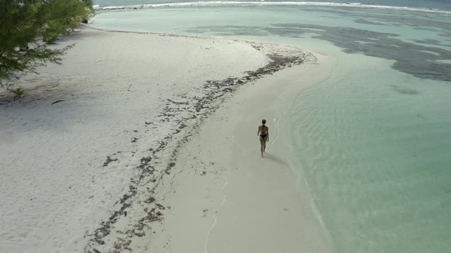Aerial: Drone moving towards woman in bikini walking on sea shore, she in on vacation at beach - Coco Plum Cay, Belize