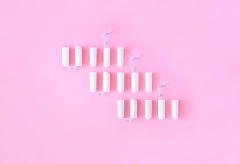 Pattern of white hygienic tampons in a vertical row on a pink background. Menstrual cycle, protective equipment, feminine hygiene. Top view, flat lay, copy space for text.
