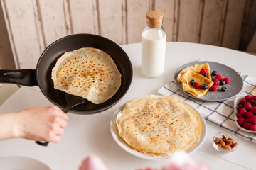 Hand of young female with frying pan taking hot appetizing pancake while cooking