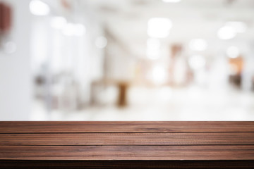 Empty wooden desk space and blurry background of white bokeh light department store for product display montage.