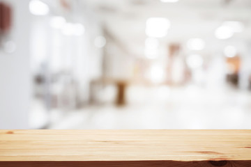 Empty wooden desk space and blurry background of white bokeh light department store for product display montage.