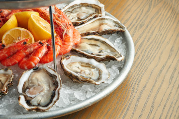 Close up view on tasty plate with seafood on ice - shrimp, oysters. Healthy Antipasti. Wooden background. Selective focus