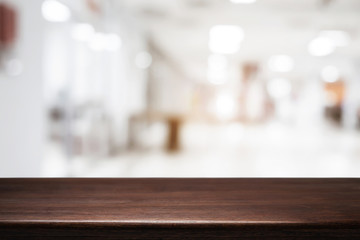 Empty wooden desk space and blurry background of white bokeh light department store for product display montage.