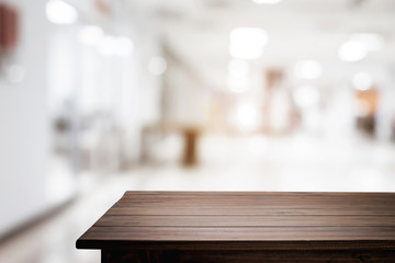 Empty wooden desk space and blurry background of white bokeh light department store for product display montage.