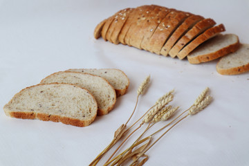 Slices of oatmeal bread and wheat ears on the background of a sliced loaf of bread